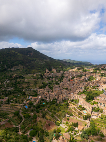 Aerial view of the historic village of Valldemossa featuring traditional stone houses and terraced gardens nestled in the lush green mountains Valldemossa Balearic Islands Spain.