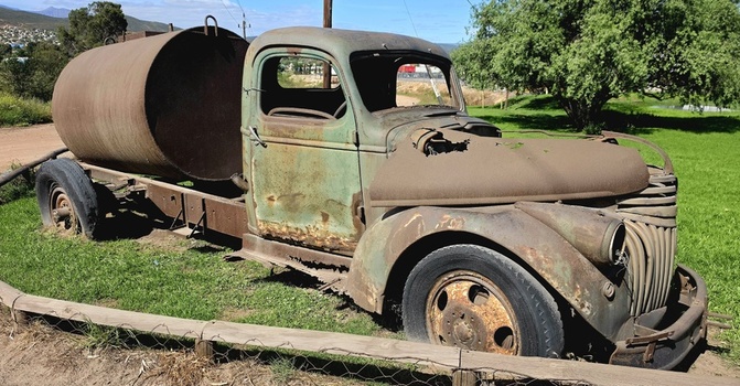 View of an abandoned vintage truck with a large metal tank featuring weathered green paint and rusted surfaces resting in a grassy field in Ladismith Western Cape South Africa.