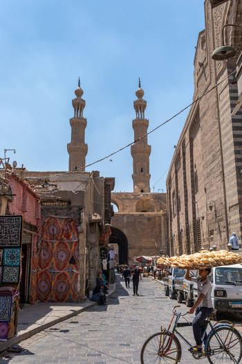 El Darb El Ahmar Egypt 20 April 2026 View of Bab Zuwayla with its twin minarets and a boy on a bicycle carrying bread on his head along a historic street. El Darb El Ahmar Egypt 20 April 2026 View of Bab Zuwayla with its twin minarets and a boy on a bicycle carrying bread on his head along a historic street.