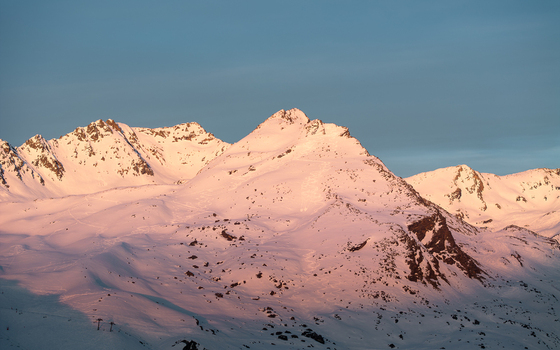 Aerial view of snow covered mountain peaks kissed by the warm glow of the setting sun against a cool blue sky Val Thorens Auvergne Rh&ocirc;ne Alpes France.