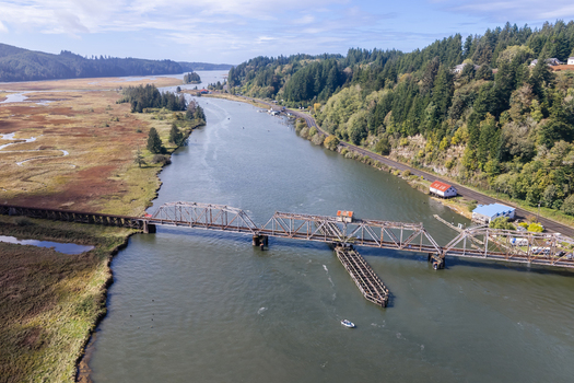 Aerial view of the historic Siuslaw River Train Bridge spanning the river surrounded by lush green forests wetlands and a small boat on the water in Florence Oregon United States.