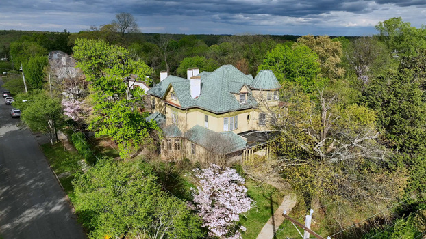 Aerial view of a historic house with a green roof surrounded by lush spring trees and a blooming dogwood in a residential neighborhood in Lynchburg Virginia United States.