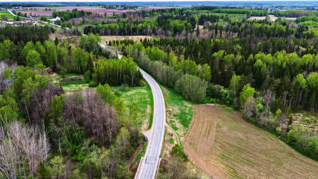 Aerial view of a winding road cutting through a dense green forest and open agricultural fields in the countryside of Latvija. Aerial view of a winding road cutting through a dense green forest and open agricultural fields in the countryside of Latvija.