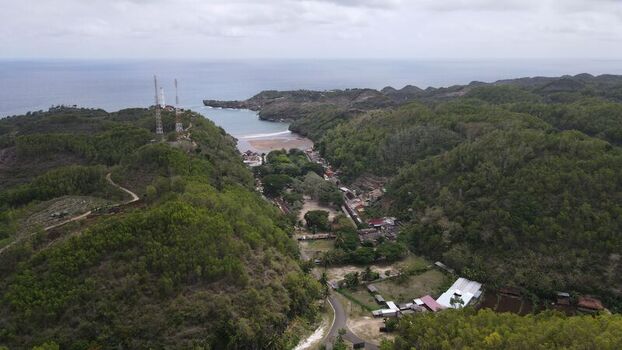 Aerial view of Baron Beach with its sandy cove surrounding lush green hills communication towers and coastal vegetation in Tanjungsari Special Region of Yogyakarta Indonesia. Aerial view of Baron Beach with its sandy cove surrounding lush green hills communication towers and coastal vegetation in Tanjungsari Special Region of Yogyakarta Indonesia.