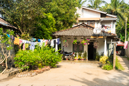 View of a traditional two story house with a motorcycle parked in front laundry hanging on a line and lush tropical greenery in Galle Southern Province Sri Lanka.