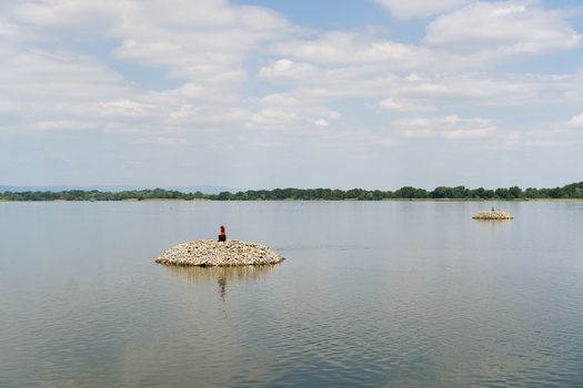 View of a person in red sitting on a small stone island in the middle of a calm river under a cloudy sky Bratislava Bratislava Region Slovakia. View of a person in red sitting on a small stone island in the middle of a calm river under a cloudy sky Bratislava Bratislava Region Slovakia.