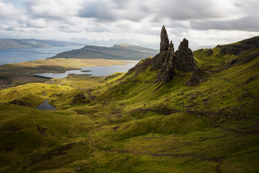 View of the iconic rock pinnacles of The Storr overlooking rolling green hills and Loch Leathan under a dramatic cloudy sky in Portree Scotland United Kingdom.