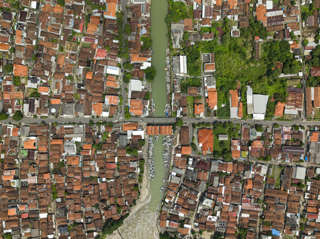 Aerial view of a river cutting through a dense urban landscape with vibrant red tiled roofs contrasting against the green river and trees Jepara Central Java Indonesia.