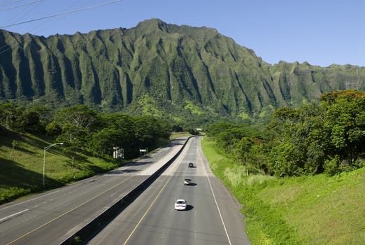 View of the H 3 highway winding through the lush green Koolau Range mountains with cars driving along the road in Kaneohe Hawaii United States.
