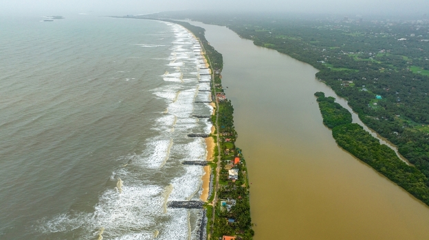 Aerial view of Mattu Beach featuring a narrow strip of land separating the Arabian Sea from the backwaters with breakwaters palm trees and coastal houses in Udupi Karnataka India.