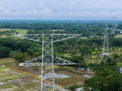 Trishal Upazila Bangladesh 13 May 2026 Aerial view of workers climbing a high voltage electricity pylon amidst lush green rural fields and trees under an overcast sky. Trishal Upazila Bangladesh 13 May 2026 Aerial view of workers climbing a high voltage electricity pylon amidst lush green rural fields and trees under an overcast sky.