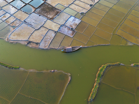 Aerial view of salt pans and geometric fields with a traditional wooden boat on a green canal in Moheskhali Upazila Chittagong Division Bangladesh. Aerial view of salt pans and geometric fields with a traditional wooden boat on a green canal in Moheskhali Upazila Chittagong Division Bangladesh.