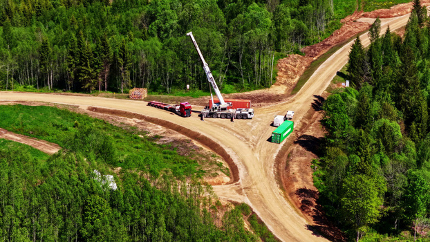 Aerial view of a crane truck and shipping containers at a dirt road junction in a forest serving as a wind turbine maintenance road in Latvija. Aerial view of a crane truck and shipping containers at a dirt road junction in a forest serving as a wind turbine maintenance road in Latvija.