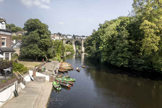 View of the River Nidd with colorful rowboats moored at the bank and the historic railway viaduct in the background in Knaresborough England United Kingdom.