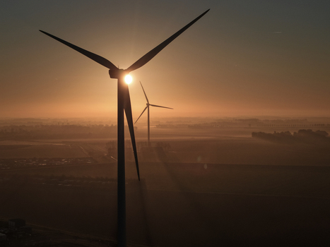 Aerial view of wind turbines silhouetted against a golden sunrise with misty fields in the background in Vrouwenpolder Zeeland Netherlands.
