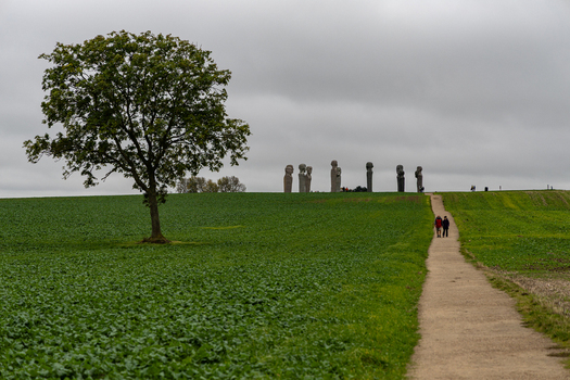 View of the Dodekalitten stone sculptures standing on a hill with a large tree in the foreground and a path leading towards them in Kragenaes Lolland Denmark. View of the Dodekalitten stone sculptures standing on a hill with a large tree in the foreground and a path leading towards them in Kragenaes Lolland Denmark.