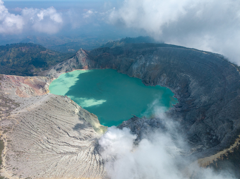 Aerial view of Ijen crater lake with its turquoise water rugged volcanic slopes and surrounding clouds in Ijen East Java Indonesia.