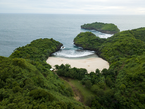Aerial view of Sedahan Beach s secluded cove embraced by verdant cliffs meeting the turquoise sea under a soft sky Gunungkidul Regency Special Region of Yogyakarta Indonesia. Aerial view of Sedahan Beach s secluded cove embraced by verdant cliffs meeting the turquoise sea under a soft sky Gunungkidul Regency Special Region of Yogyakarta Indonesia.