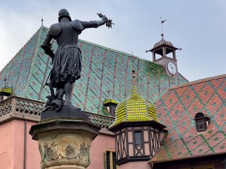 View of the bronze statue of Admiral Bruat standing before the historic Koifhus with its iconic colorful tiled roof and clock tower in Colmar Grand Est France.