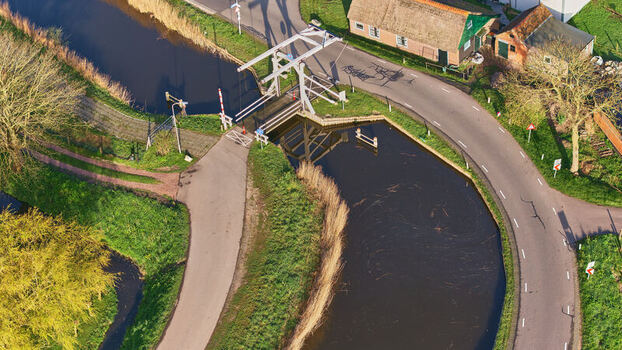Aerial view of the historic Wipbrug drawbridge and a traditional thatched roof house along a winding canal in the countryside Spanbroek North Holland Netherlands.