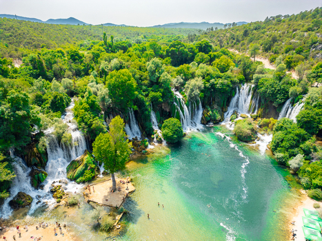 Aerial view of Kravica Waterfall with cascading water lush green trees and people swimming in the turquoise pool in Zvirici Federation of Bosnia Bosnia and Herzegovina. Aerial view of Kravica Waterfall with cascading water lush green trees and people swimming in the turquoise pool in Zvirici Federation of Bosnia Bosnia and Herzegovina.