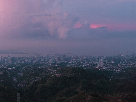 Aerial view of the city skyline and lush hills of Busay under a purple sunset sky in Cebu City Central Visayas Philippines.
