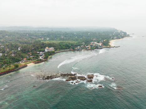 Aerial view of the tropical coastline with turquoise water rocky formations and lush green forest in Unawatuna Southern Province Sri Lanka.