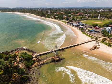 Aerial view of the coastline with a wooden bridge leading to a small island sandy beach and turquoise ocean waves Matara Southern Province Sri Lanka. Aerial view of the coastline with a wooden bridge leading to a small island sandy beach and turquoise ocean waves Matara Southern Province Sri Lanka.