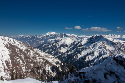 View of snow covered peaks piercing the crisp blue sky with scattered trees adding a touch of green to the wintry landscape Haveli Azad Kashmir Pakistan.