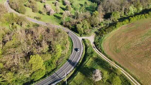 Aerial view of a car on a winding road through green hills Slovakia.