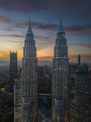 Kuala Lumpur Malaysia 11 March 2026 Aerial view of the Petronas Twin Towers illuminated at sunset with a colorful sky and city skyline in the background.