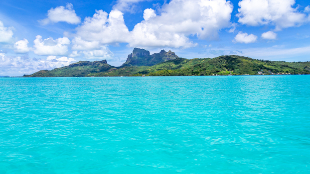 View of Mount Otemanu rising above the turquoise lagoon with lush green slopes and a bright blue sky with scattered clouds Bora Bora Leeward Islands French Polynesia.