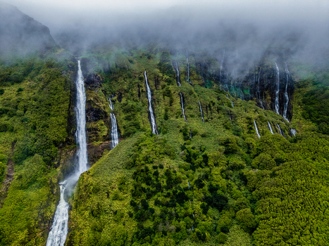 Aerial view of multiple waterfalls cascading down a verdant cliff face shrouded in mist creating a serene ethereal landscape Flores Azores Portugal.