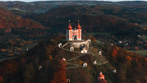 Aerial view of the Kalvaria Banska Stiavnica baroque church on a hill surrounded by vibrant autumn forests during golden hour in Banska Stiavnica Banskobystricky kraj Slovakia.