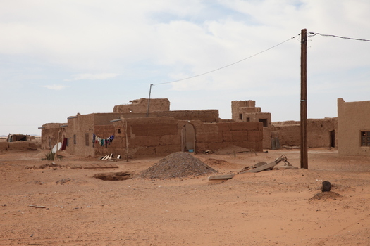 View of traditional mud brick buildings in a desert landscape with laundry hanging on a line and a utility pole in Morocco.
