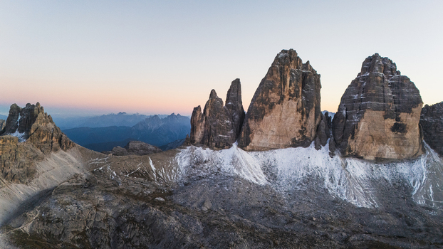 Aerial view of the iconic Tre Cime di Lavaredo peaks with snow dusted slopes and jagged rock formations under a soft twilight sky in Auronzo di Cadore Veneto Italy. Aerial view of the iconic Tre Cime di Lavaredo peaks with snow dusted slopes and jagged rock formations under a soft twilight sky in Auronzo di Cadore Veneto Italy.