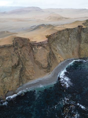 Aerial view of the Reserva Nacional de Paracas with steep rocky cliffs overlooking the dark ocean and vast desert landscape Paracas Ica Peru.