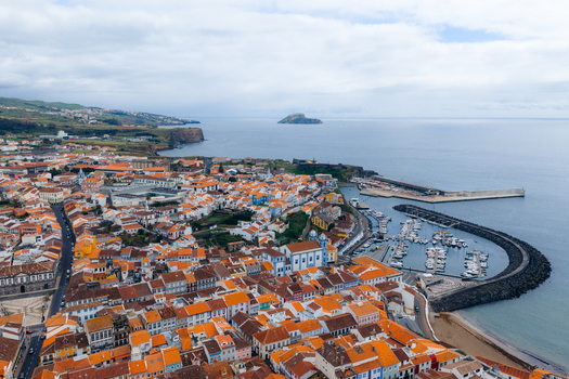 Aerial view of the historic center with orange tiled rooftops the harbor filled with boats and the blue Igreja da Misericordia church in Angra do Heroismo Azores Portugal.