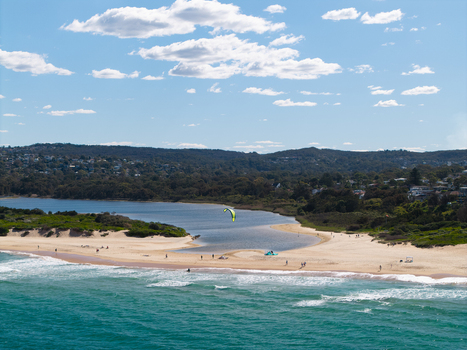 Aerial view of a kite surfer on the beach at the lagoon entrance with surrounding coastal vegetation and residential areas in Northern Beaches Council New South Wales Australia.