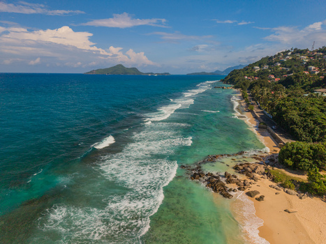 Aerial view of turquoise waves gently kissing the golden sands lush green hills meeting the azure sky La Retraite Mahe Island Seychelles. Aerial view of turquoise waves gently kissing the golden sands lush green hills meeting the azure sky La Retraite Mahe Island Seychelles.