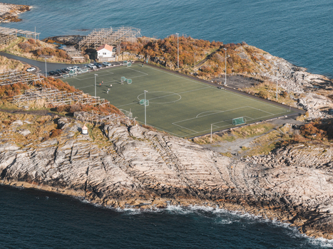Aerial view of the soccer field in Lofoten surrounded by rocky coastline sea and wooden fish drying racks in Leknes Nordland Norway. Aerial view of the soccer field in Lofoten surrounded by rocky coastline sea and wooden fish drying racks in Leknes Nordland Norway.