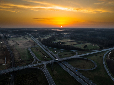 Aerial view of the A5 and A8 highway interchange at sunset featuring sweeping ramps and roads surrounded by fields and forests in Olaine parish Olaine Municipality Latvia. Aerial view of the A5 and A8 highway interchange at sunset featuring sweeping ramps and roads surrounded by fields and forests in Olaine parish Olaine Municipality Latvia.