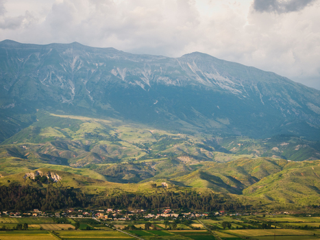 Aerial view of the rugged mountain peaks and lush green rolling hills overlooking a small village and agricultural fields in Gjirokaster Gjirokaster County Albania. Aerial view of the rugged mountain peaks and lush green rolling hills overlooking a small village and agricultural fields in Gjirokaster Gjirokaster County Albania.