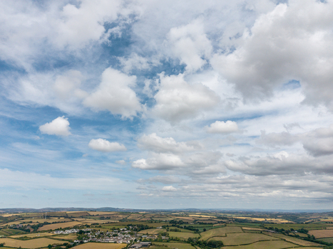 Aerial view of rural landscape featuring patchwork agricultural fields hedgerows and rolling hills under a bright sky with scattered clouds in Looe Cornwall United Kingdom. Aerial view of rural landscape featuring patchwork agricultural fields hedgerows and rolling hills under a bright sky with scattered clouds in Looe Cornwall United Kingdom.