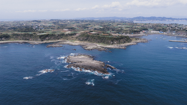 Aerial view of a rocky island surrounded by deep blue sea with a rugged coastline and agricultural fields in the background Japan. Aerial view of a rocky island surrounded by deep blue sea with a rugged coastline and agricultural fields in the background Japan.