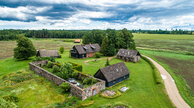 Aerial view of a traditional rural farmstead in Latvia featuring historic stone buildings wooden barns and lush green fields under a dramatic cloudy sky Latvia. Aerial view of a traditional rural farmstead in Latvia featuring historic stone buildings wooden barns and lush green fields under a dramatic cloudy sky Latvia.