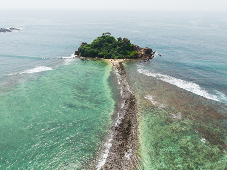 Aerial view of Devil s Rock island connected by a narrow reef to the coast with turquoise ocean waves Ahangama Southern Province Sri Lanka. Aerial view of Devil s Rock island connected by a narrow reef to the coast with turquoise ocean waves Ahangama Southern Province Sri Lanka.