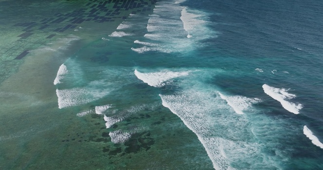 Aerial view of ocean waves breaking over a coral reef with seaweed farming plots in the turquoise shallows off the coast of Lombok West Nusa Tenggara Indonesia.