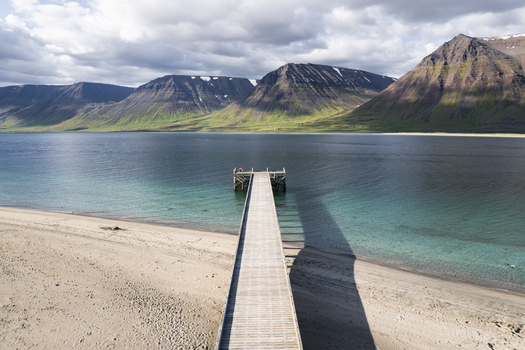 Aerial view of Onundarfjordur Pier extending into the turquoise water from a sandy beach with dramatic mountains in the background Holt Isafjardarbaer Iceland. Aerial view of Onundarfjordur Pier extending into the turquoise water from a sandy beach with dramatic mountains in the background Holt Isafjardarbaer Iceland.