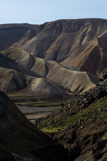 View of rugged terrain with stark contrasts of dark rocks and golden hills under a clear sky creating a dramatic landscape Rang&aacute;r&thorn;ing ytra Iceland.